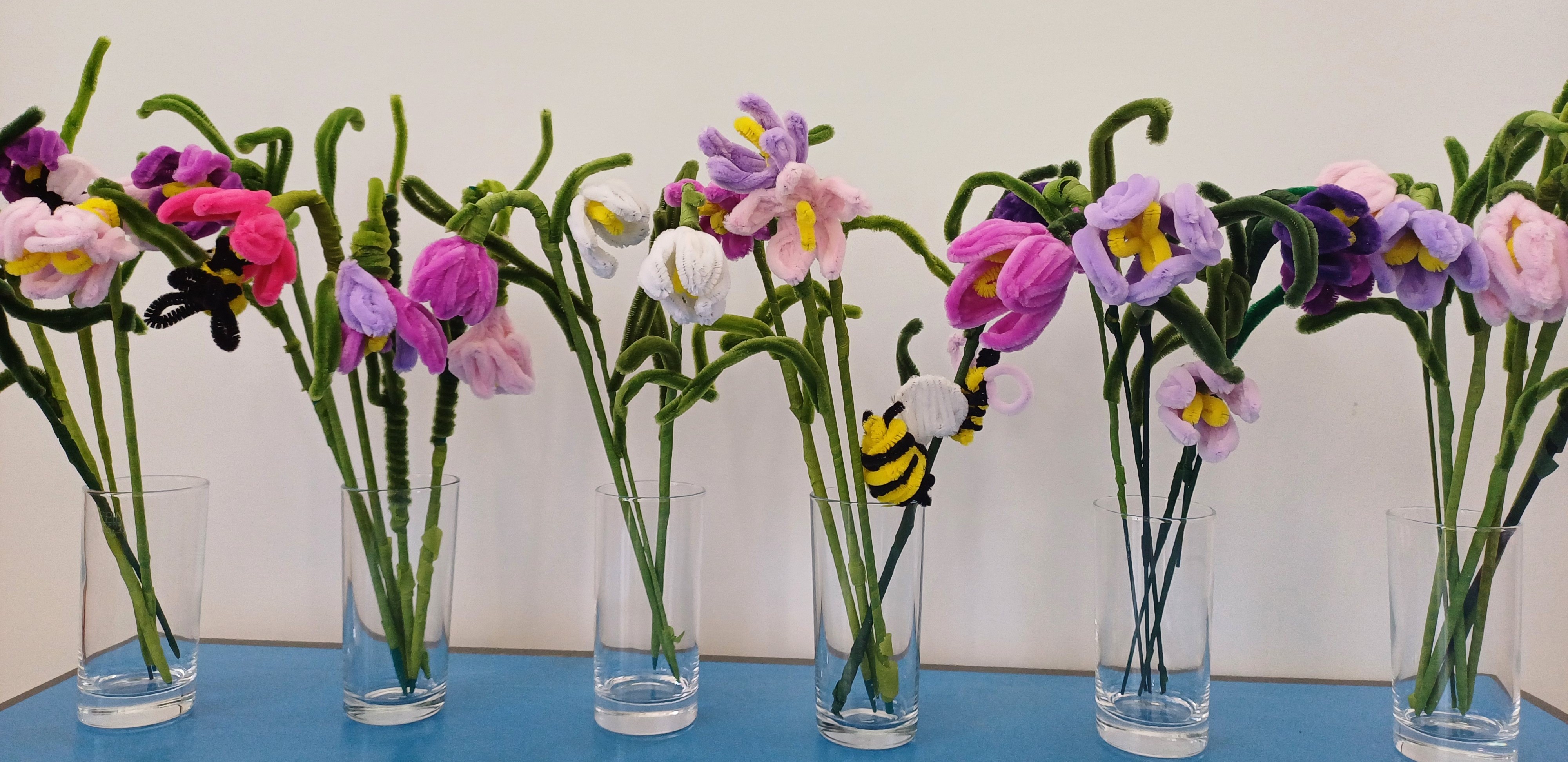 A row of snake's-head fritillary flowers made from pipecleaners in vases