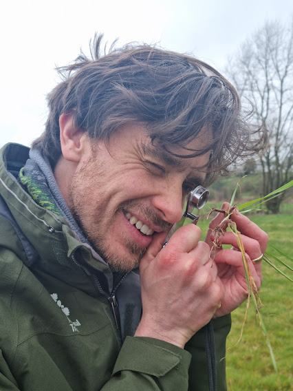 Photo of a researcher examining grass with an eye glass